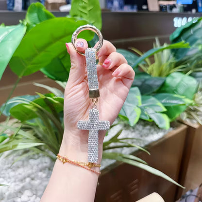 Hand holding a diamond-encrusted keychain with plants in the background