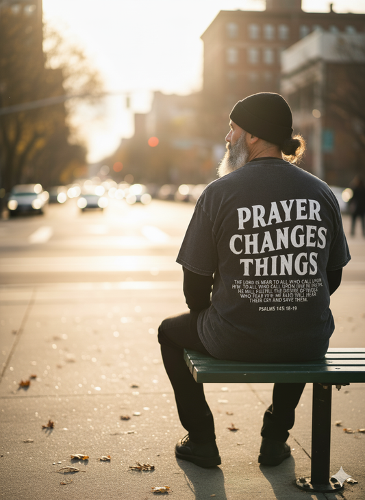 Person sitting on a bench wearing a t-shirt with 'PRAYER CHANGES THINGS' text.